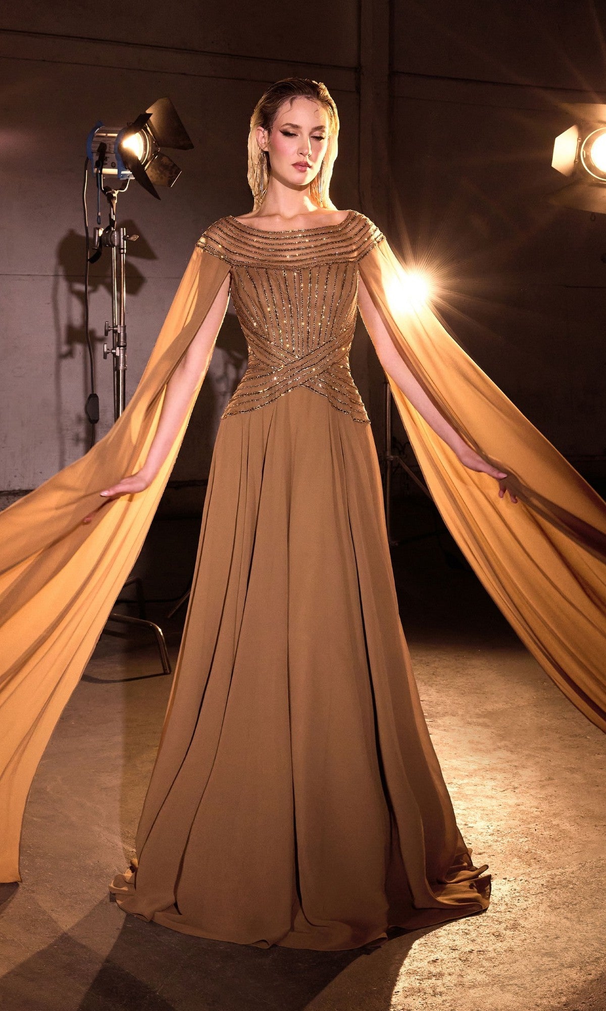 A woman poses in a studio wearing the Cape-Sleeve Long Bronze Formal Dress: Ladivine CL08, a floor-length gown featuring beaded details and dramatic cape sleeves under studio lights.